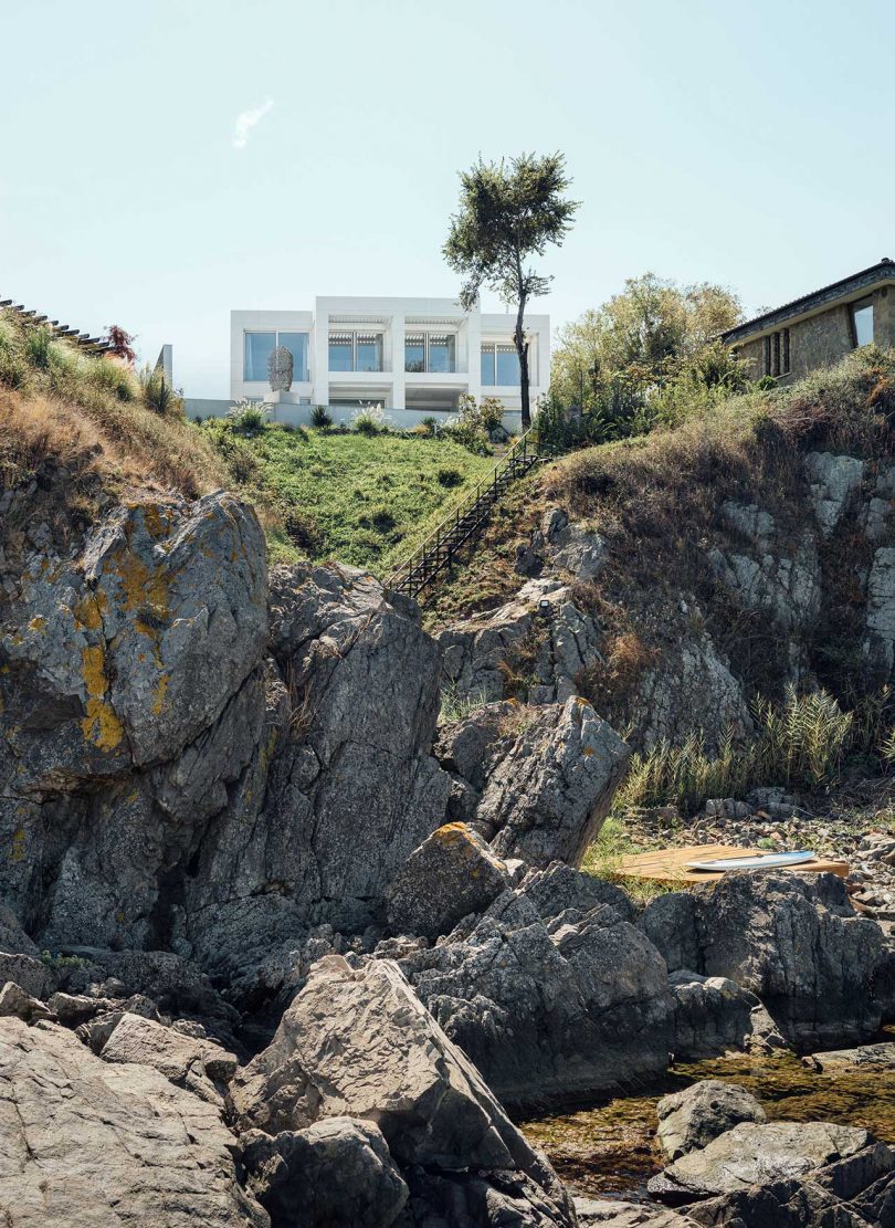 vista exterior de una casa moderna minimalista, completamente blanca, en lo alto de un acantilado rocoso 