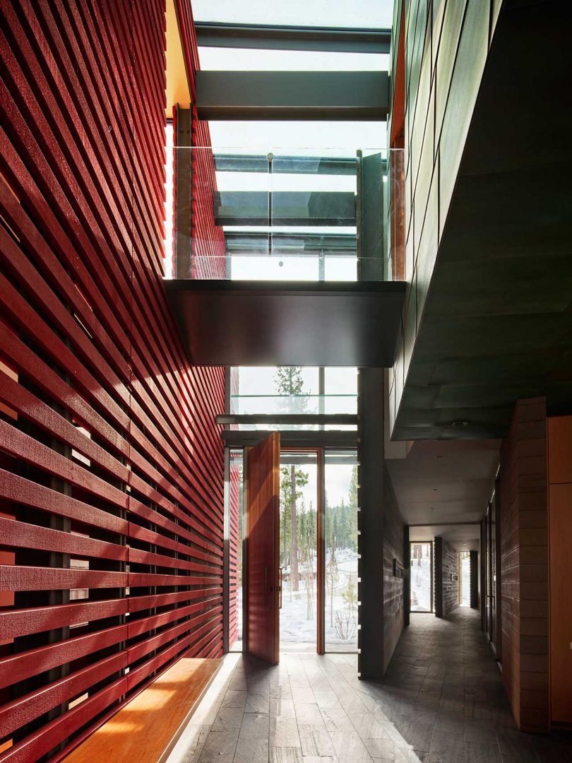 toma interior de un largo pasillo de una casa moderna con una gran pared de listones rojos y tragaluces