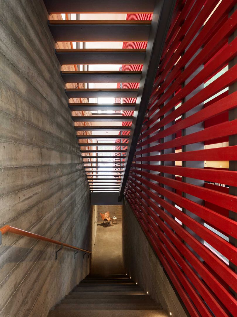 un conjunto de escaleras que conducen al sótano con escaleras abiertas en la parte superior y una pared de listones rojos a un lado