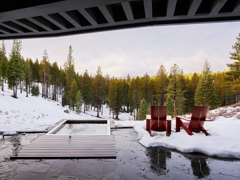 cubierta de patio de una casa moderna con vistas a una bañera de hidromasaje y dos sillas rojas a un paisaje nevado