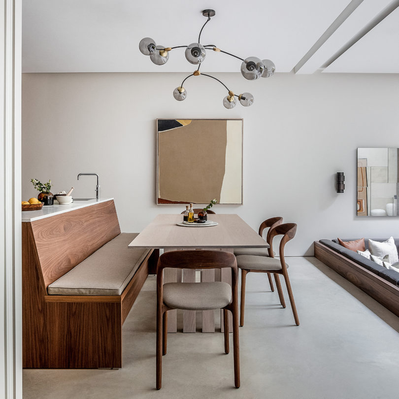 mesa de comedor interior estilizada con sillas y banco, obras de arte e iluminación de araña de techo