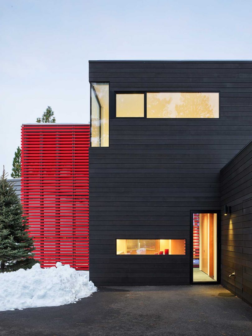 Una toma exterior nevada de una casa moderna con un volumen con persianas negras y un volumen con persianas rojas